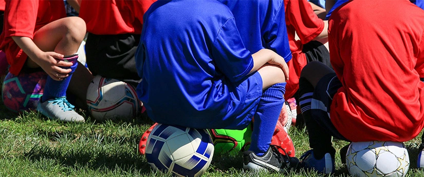 çimlerdeki futbol toplarının üzerine oturan çocuklar